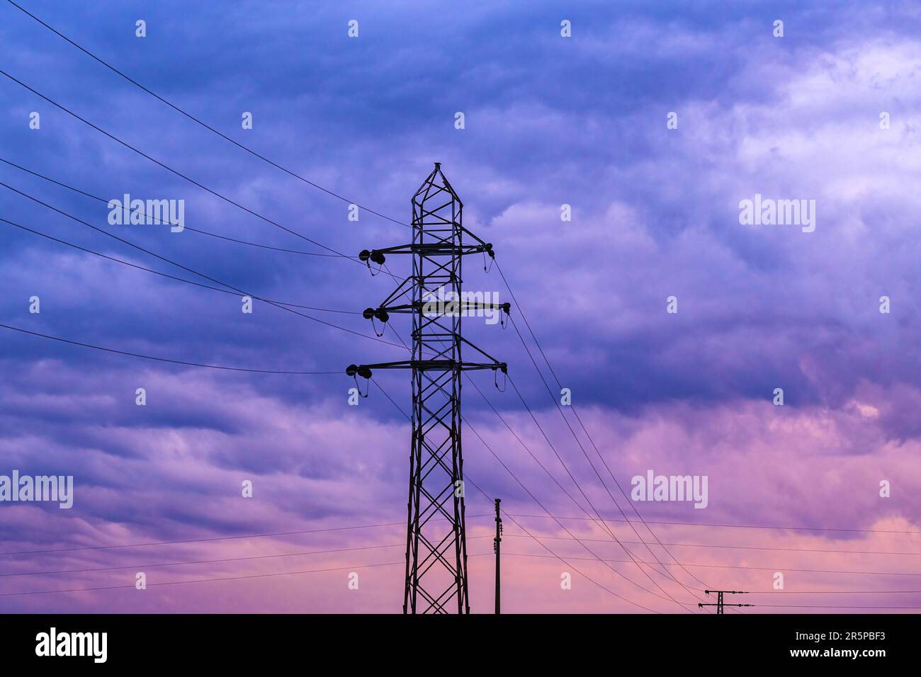 Energiegeladene Krisensituation konzeptionelles Bild, Silhouette von Strommasten und Stromkabeln vor dem dramatischen violetten Sonnenuntergang Himmel, selektiver Fokus Stockfoto
