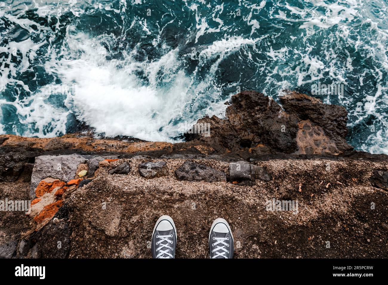 Suizidgedanken oder -Gedanken, junge Person, die an der Meeresklippe über dem kalten Wasser steht und Meeresschaum, nachdem Wellen an Felsen krachen, pov-Bild Stockfoto
