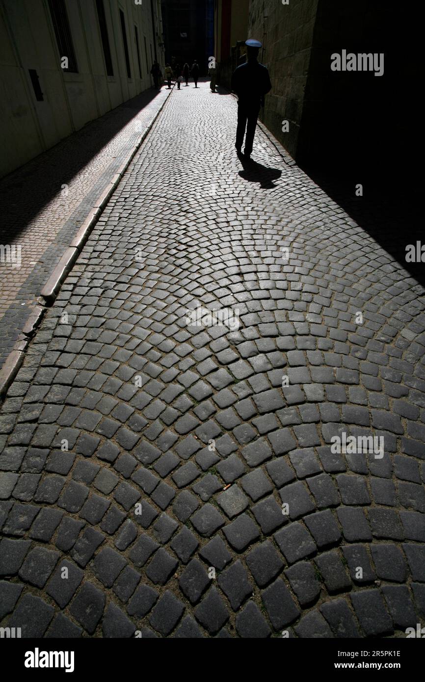 Kopfsteinpflasterstraße in Mala Strana, Prag, Tschechische Republik, mit einer einsamen Figur eines Mannes in blauer Uniform, der wegläuft Stockfoto