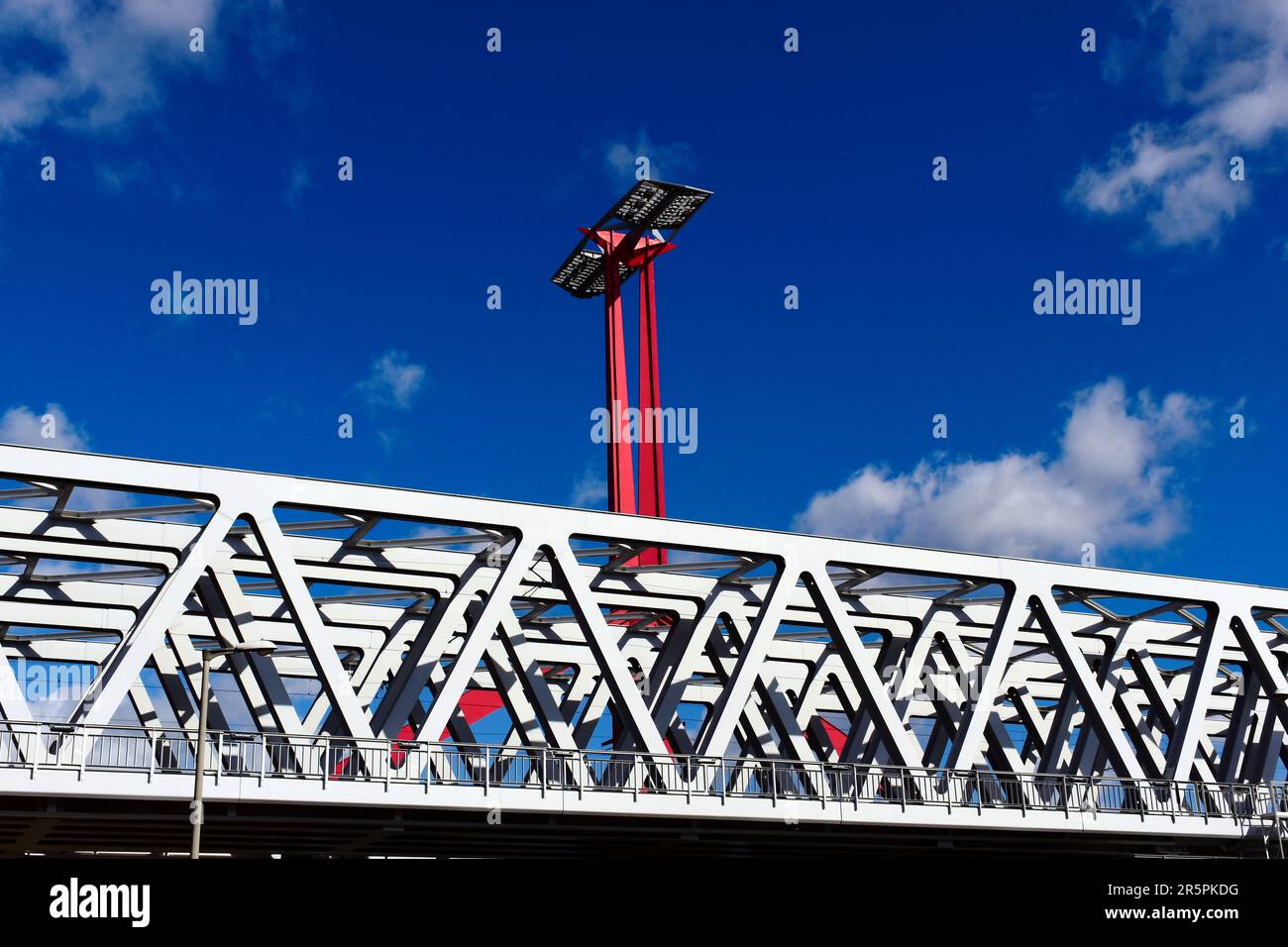 Nahaufnahme der Stahlbahnbrücke aus perspektivischer Sicht. Roter Stahlturm mit Sonnenkollektoren. Blauer Himmel mit weißen Wolken. Stabbalken mit dreieckigen Elementen Stockfoto
