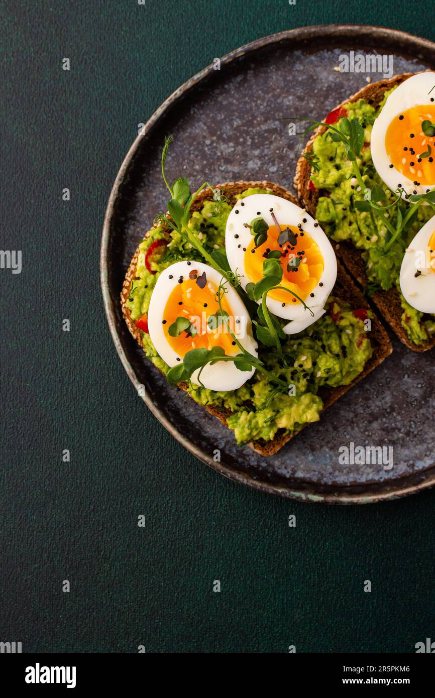 Sandwiches mit Roggenbrot und Guacamole, gekochten Eiern und Grünen aus Erbsen und Radieschen sowie Sesamsamen, ein Teller mit Sandwiches aus nächster Nähe Stockfoto