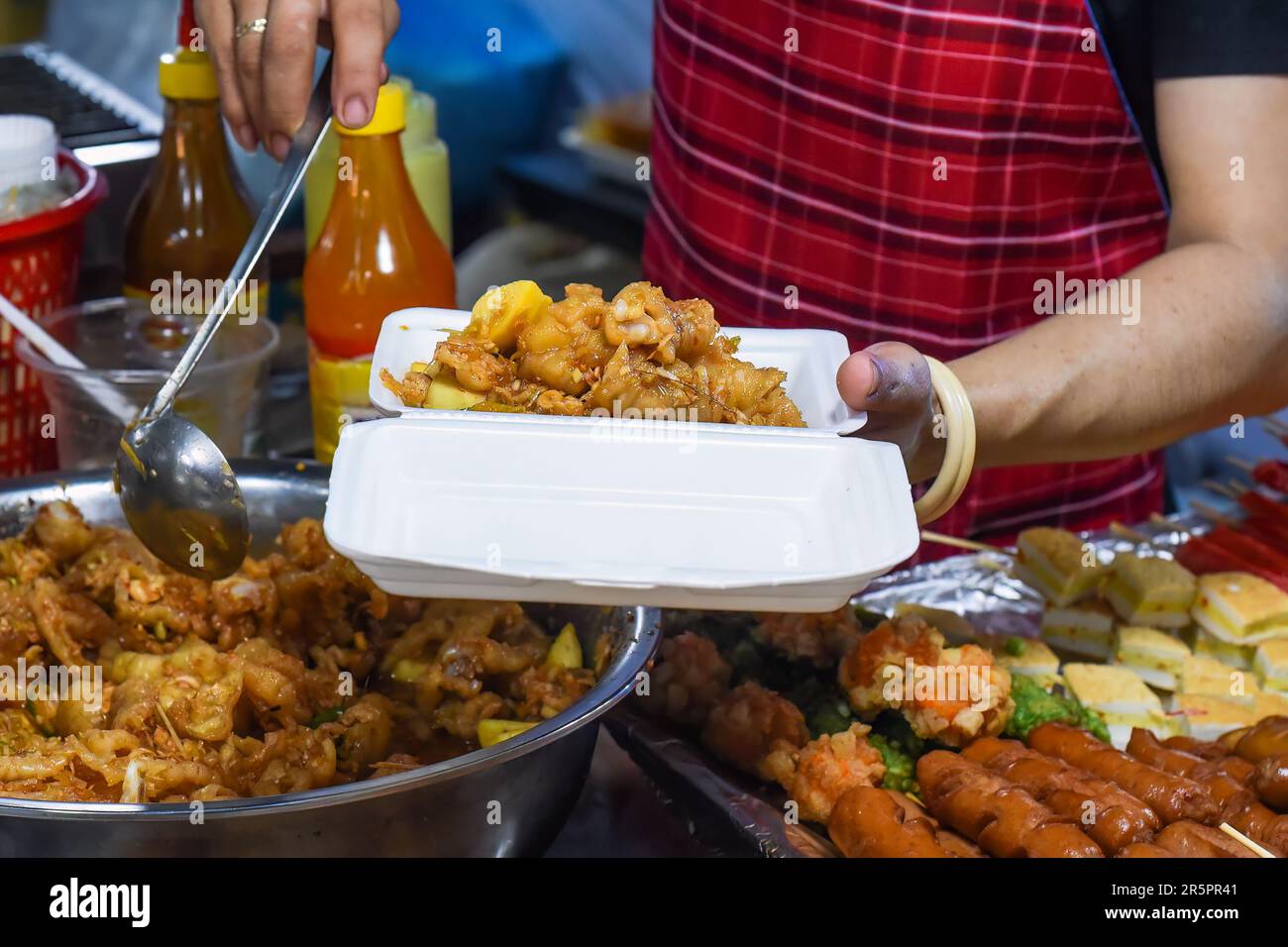 Vietnamesische Frau serviert Hühnerpfoten in einer Plastikbox mit Chili auf dem vietnamesischen Nachtmarkt Stockfoto