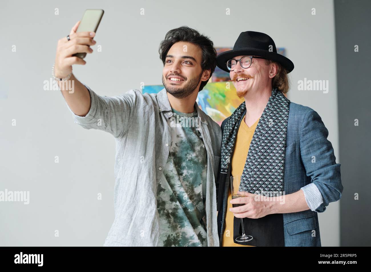 Junger Mann, der während seines Besuchs in der Kunstgalerie mit einem berühmten Künstler ein Selfie-Porträt auf seinem Smartphone macht Stockfoto