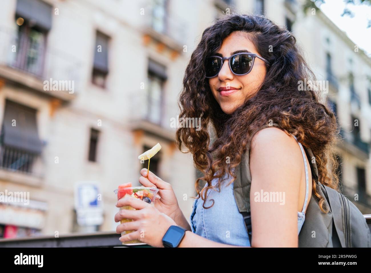Junger türkischer Reisender mit Rucksack und Sonnenbrille, der eine Tasse frisches Obst auf der Straße hält Stockfoto