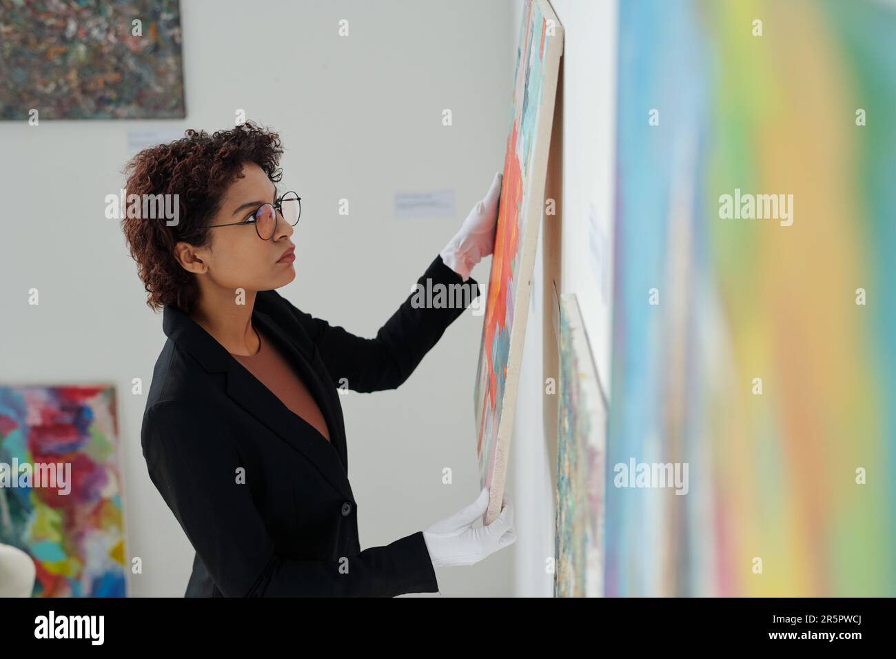 Junger Galeriebesitzer in weißen Handschuhen, der in der Galerie Gemälde an die Wand hängt Stockfoto