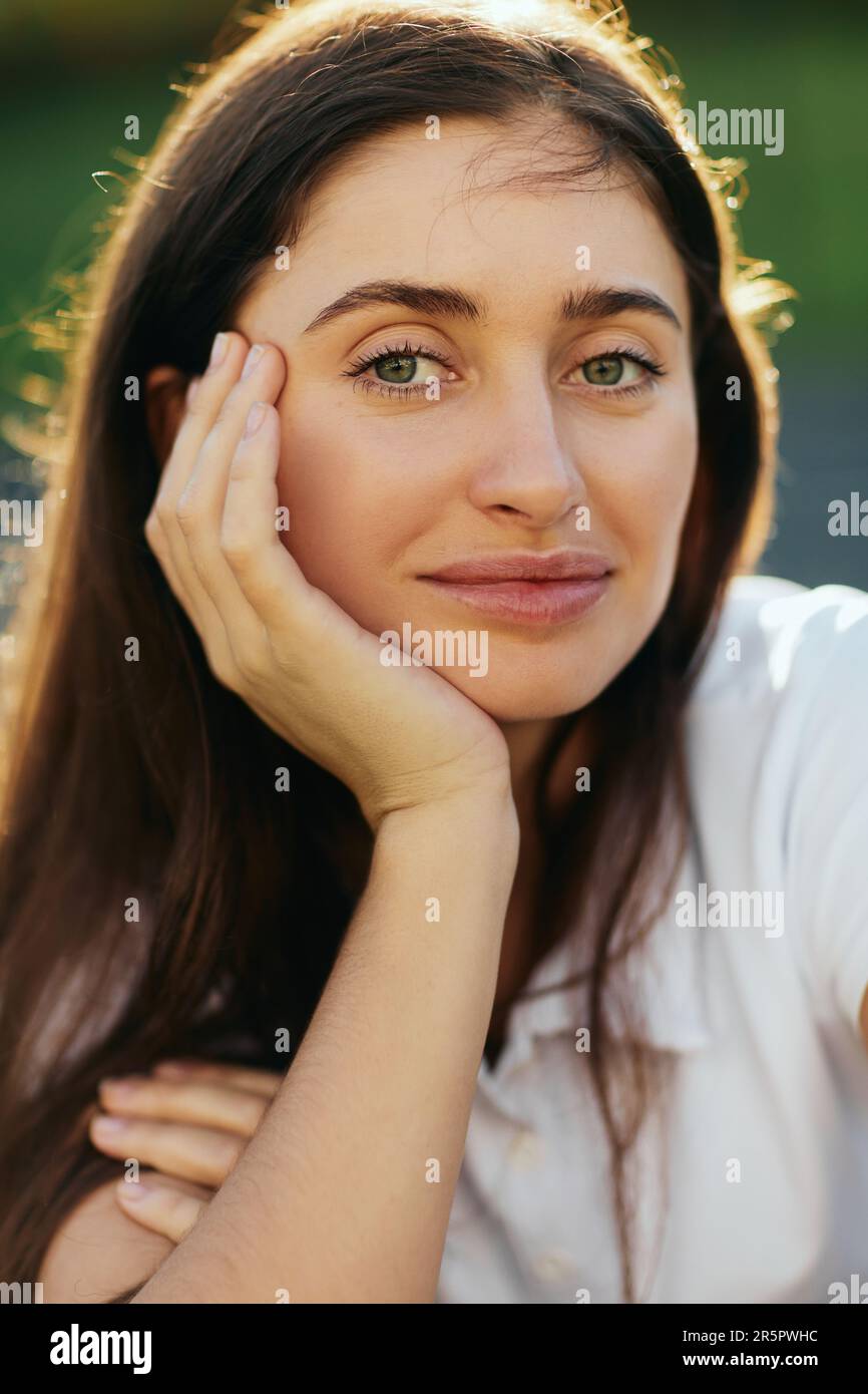 Porträt einer entzückenden jungen Frau mit braunem, langem Haar, posiert in weißem Poloshirt und schaut in die Kamera, verschwommener Hintergrund, Miami, Florida, Iconi Stockfoto