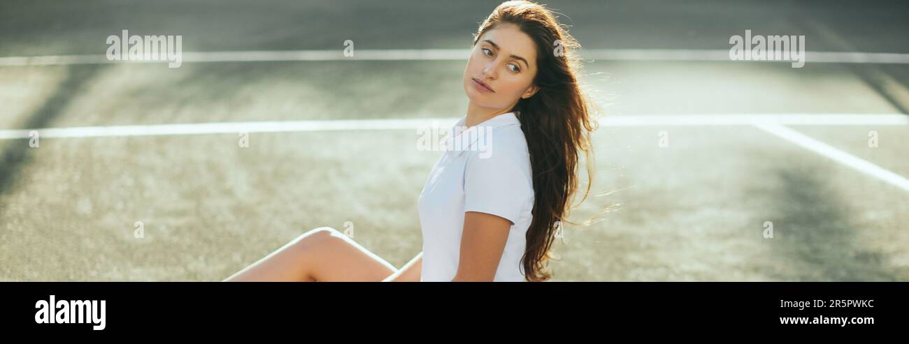 Tennisspielerin, die sich nach dem Spiel ausruht, junge Frau, die in weißem Outfit auf Asphalt sitzt und wegschaut, verschwommener Hintergrund, Miami, Tennisplatz, dow Stockfoto