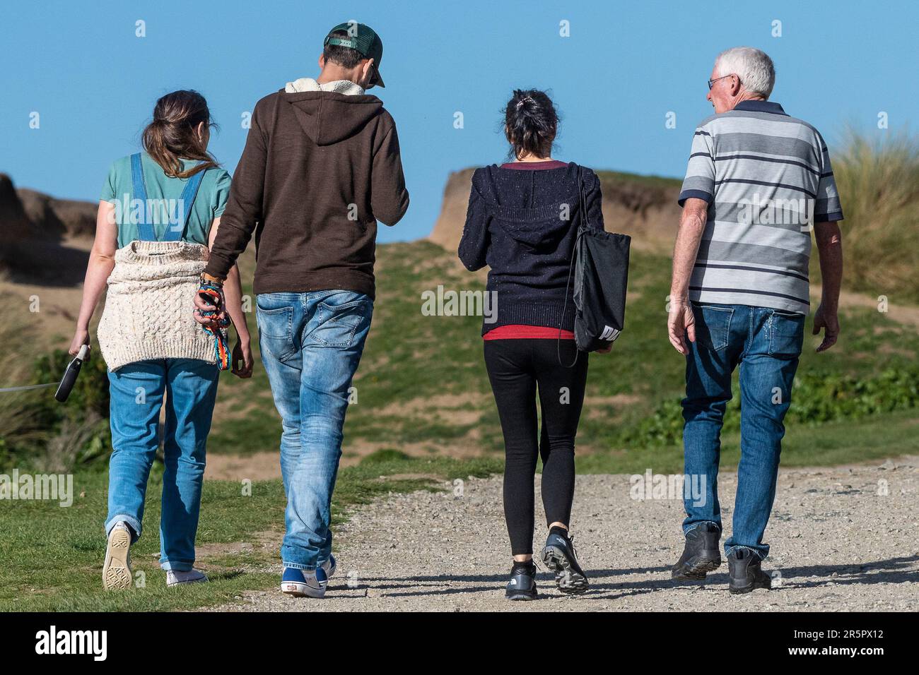 Rückansicht von vier 4-Personen, die entlang eines Küstenpfads in Newquay in Cornwall in England in Großbritannien spazieren. Stockfoto