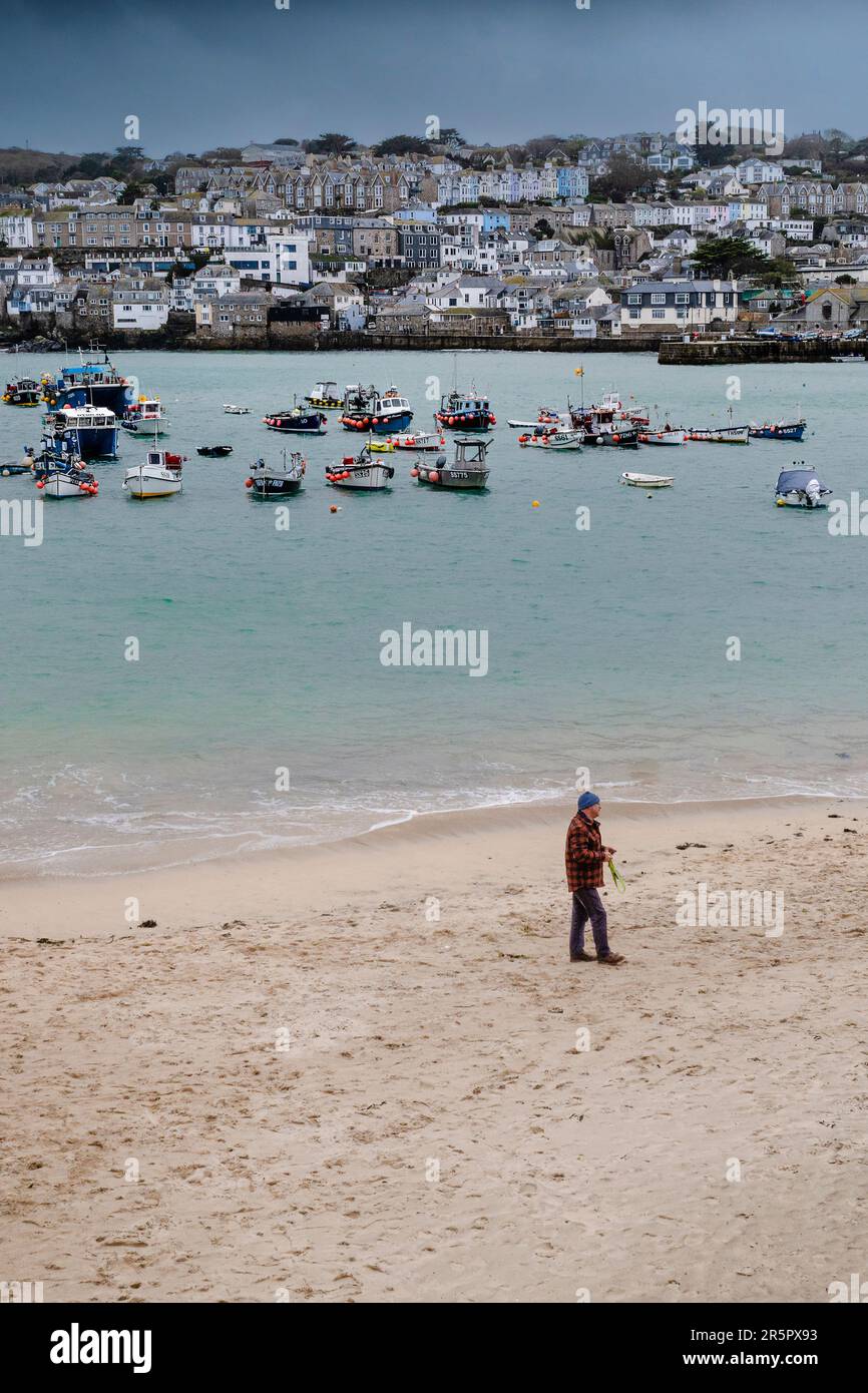 Wetter in Großbritannien. Ein Mann, der an einem regnerisch kalten, elenden Tag allein am Strand in der historischen Küstenstadt St. Ives in Cornwall in England, Großbritannien, spaziert. Stockfoto