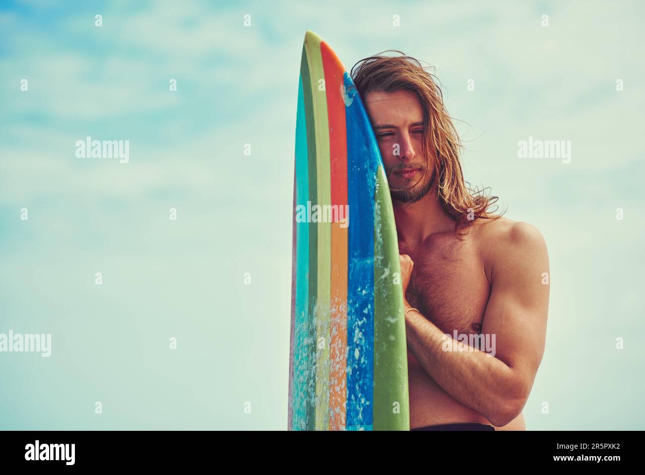 Tun Sie etwas, das alles andere irrelevant erscheinen lässt. Ein junger Surfer, der sich gegen sein Surfbrett lehnt. Stockfoto