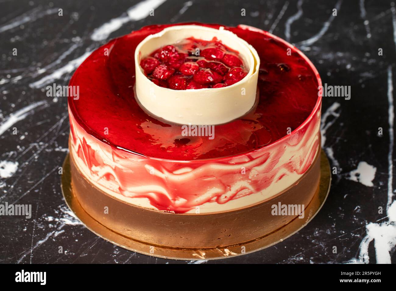 Himbeeren und weiße Schokoladenkuchen. Kuchen mit Obst und Schokoladensoße auf dunklem Hintergrund. Geburtstagskuchen oder Festtagskuchen Stockfoto