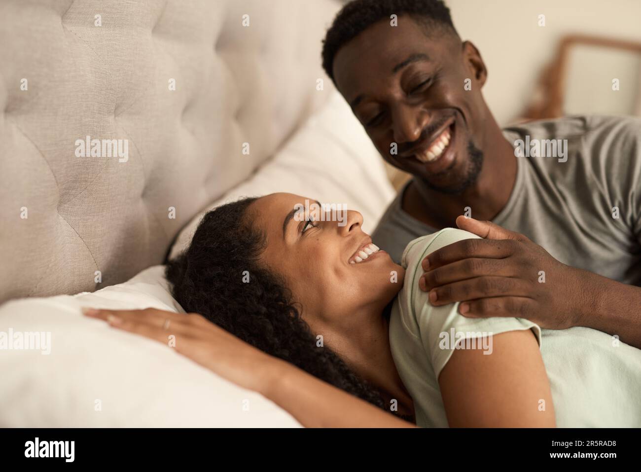 Lächelndes, junges, multiethnisches Paar, das morgens im Bett aufwacht Stockfoto