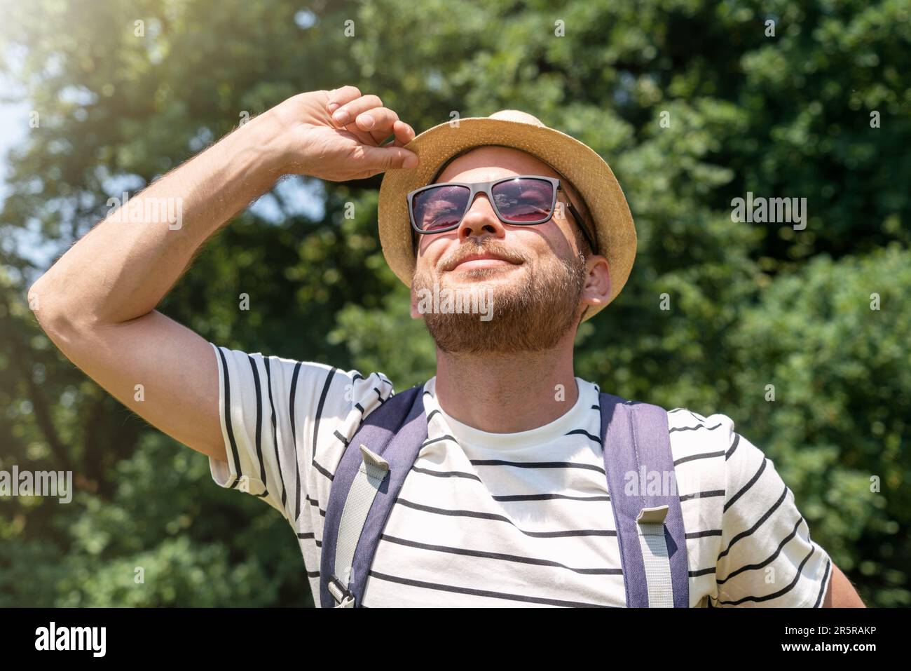 Junger erwachsener Mann mit Strohhut und Sonnenbrille, der im Sommer einen sonnigen Tag im Freien genießt. Stockfoto
