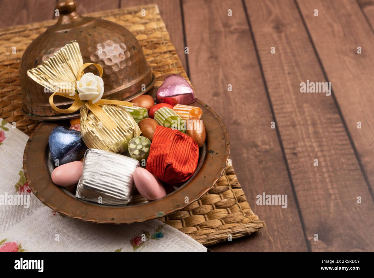 Nahaufnahme einer antiken Kupferschale mit Süßigkeiten. Gewickelte Schokolade und Mandeldragee auf dem Holztisch. Kopierbereich. ramadan Festgottesdienst. Stockfoto