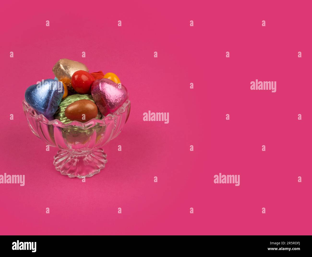 Luxuriöse Pralinen in einer Glasschale. Isolierter rosafarbener Hintergrund mit Kopierraum. Das Zuckerfest-Konzept. Mandelbonbons in stilvoller Kristallschleife. Stockfoto