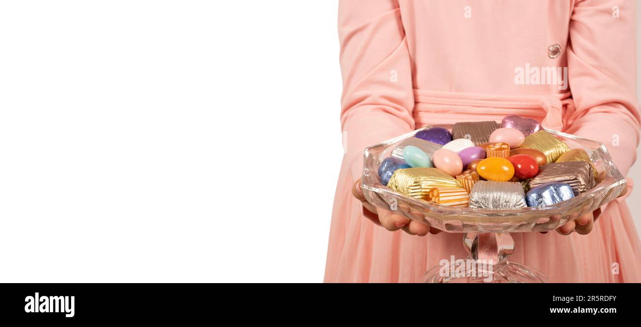 Kind hält eine Schüssel mit Süßigkeiten. Isolierter weißer Hintergrund, Kopierraum. Konzeptidee für das Zuckerfest-Banner. Weißer Hintergrund, Kopierraum. Stockfoto