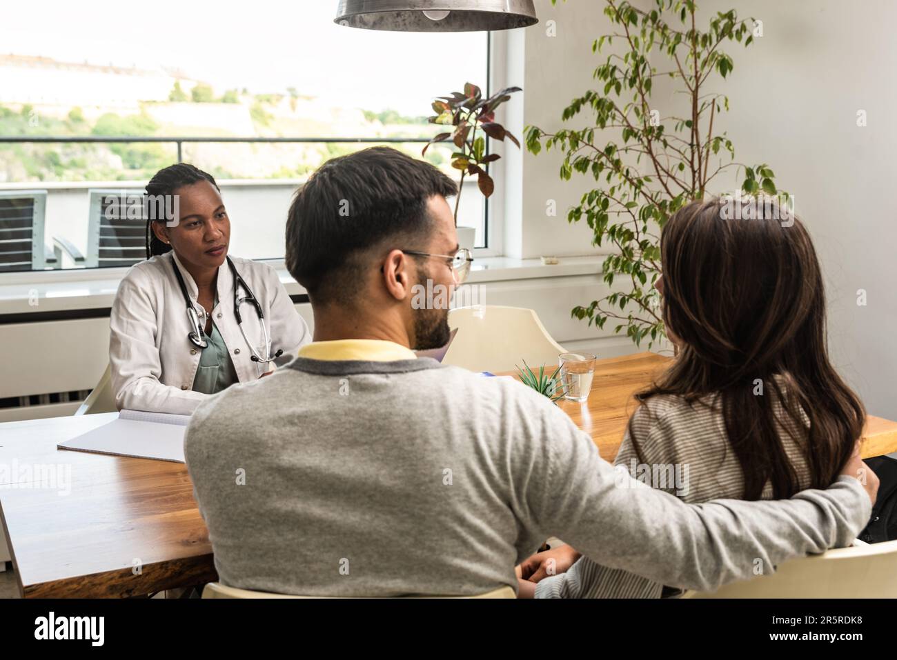 Eine Ärztin besucht ein junges Ehepaar zu Hause und gibt Gesundheitsberatungen. Arzthelferin in einer Patientenwohnung, die zuhört Stockfoto