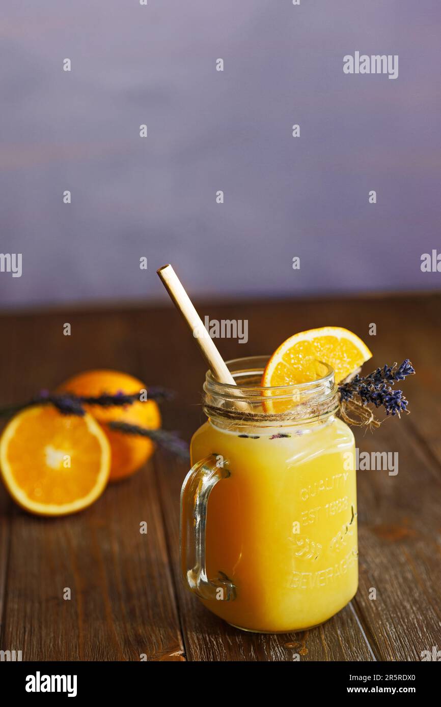 Orangefarbene Limonade in einem Becher auf einem Holztisch mit lavendelfarbenem Hintergrund Stockfoto