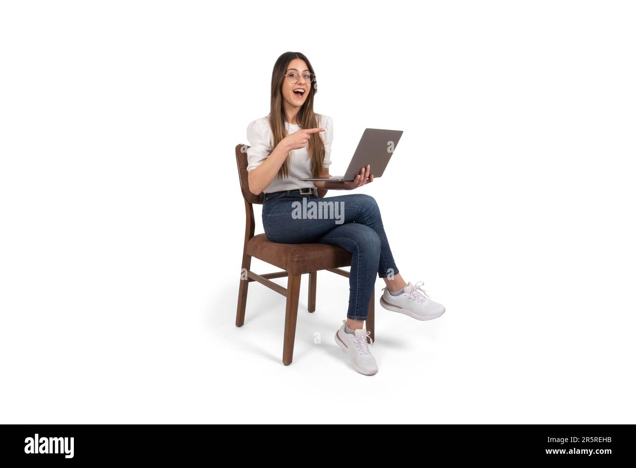 Aufgeregte kaukasische Dame, die Laptop-Frau hält, die mit dem Finger zeigt. Sitzstuhl über isoliertem weißem Hintergrund, Kopierraum. Webseite wird empfohlen. Stockfoto