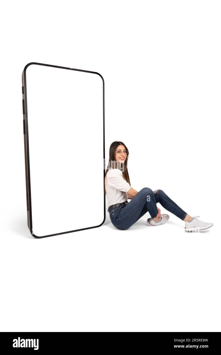 Anwendungswerbung Konzept, brünette junge Frau sitzt auf dem Boden, lehnt großes Smartphone mit leerem leeren Bildschirm Mock up. Stockfoto