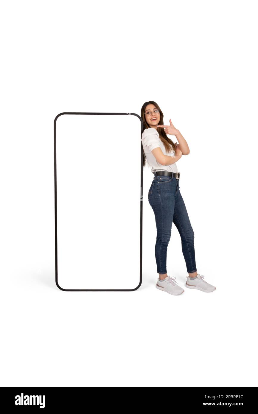 Frau, die auf ein riesiges Smartphone-Mockup mit leerem weißen Bildschirm zeigt, eine kaukasische schöne Dame, die ein riesiges Handy stützt. Stockfoto