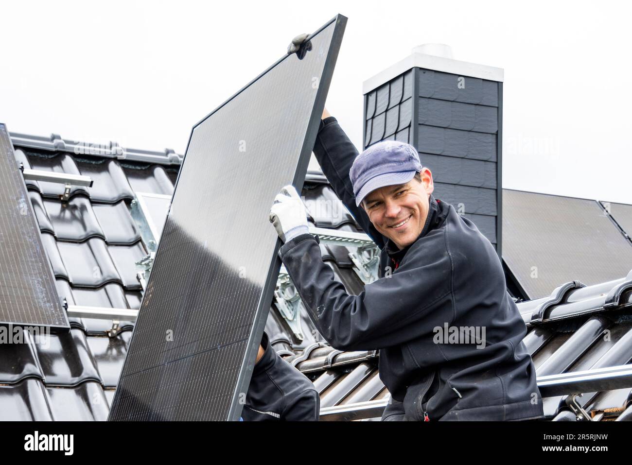 Lächelnder Handwerker, der eine Solaranlage auf einem Dach eines Hauses installiert Stockfoto