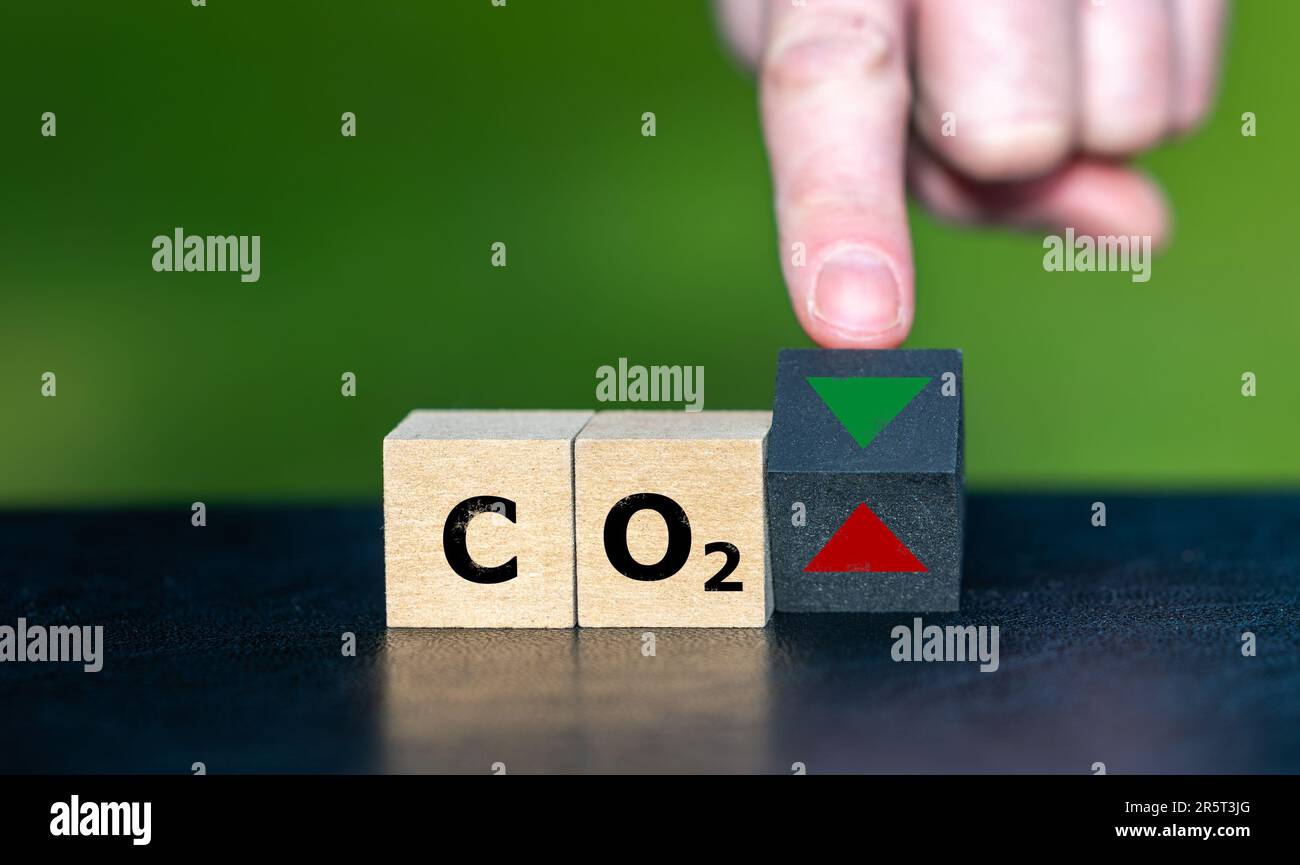 Symbol zur Reduzierung der CO2-Emissionen. Die Hand dreht einen Holzwürfel und ändert die Ausrichtung eines Pfeils von oben nach unten. Stockfoto