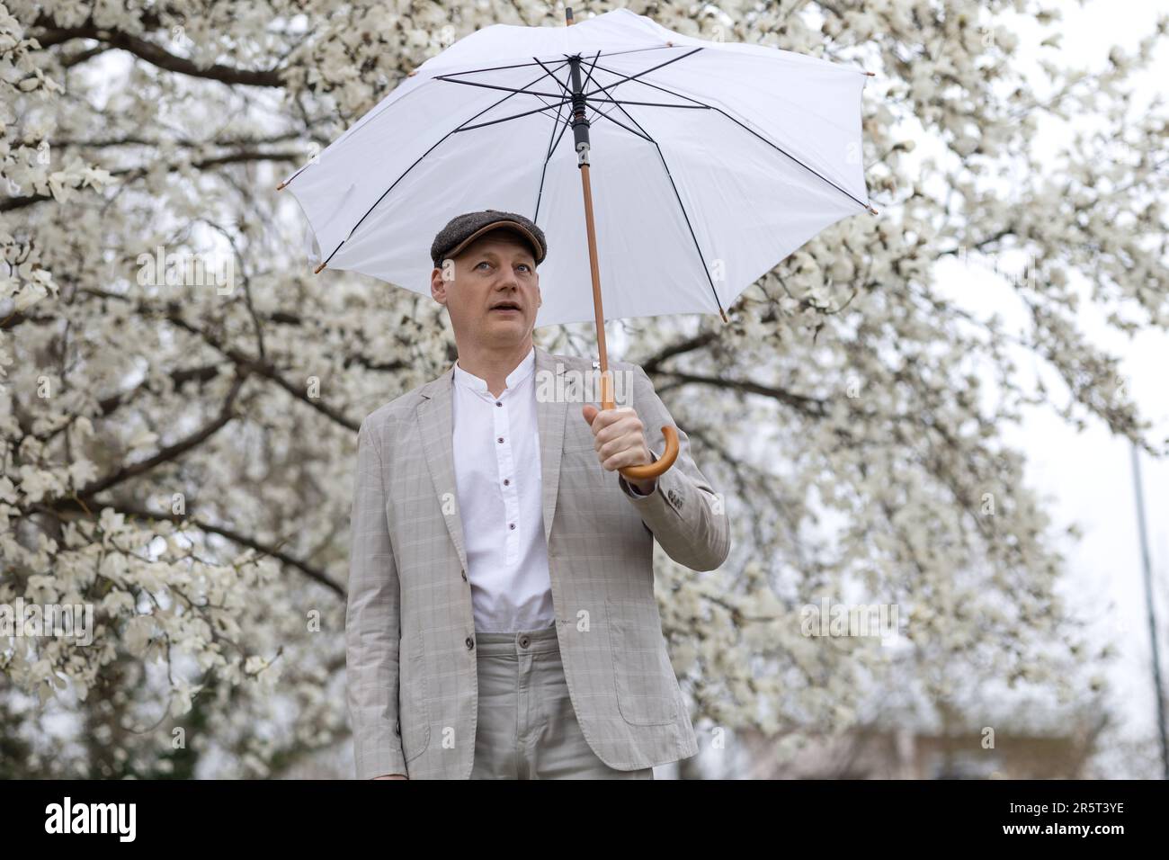 Wunderschöner lächelnder Mann mit Schirm inmitten von weißer blühender Magnolie Stockfoto