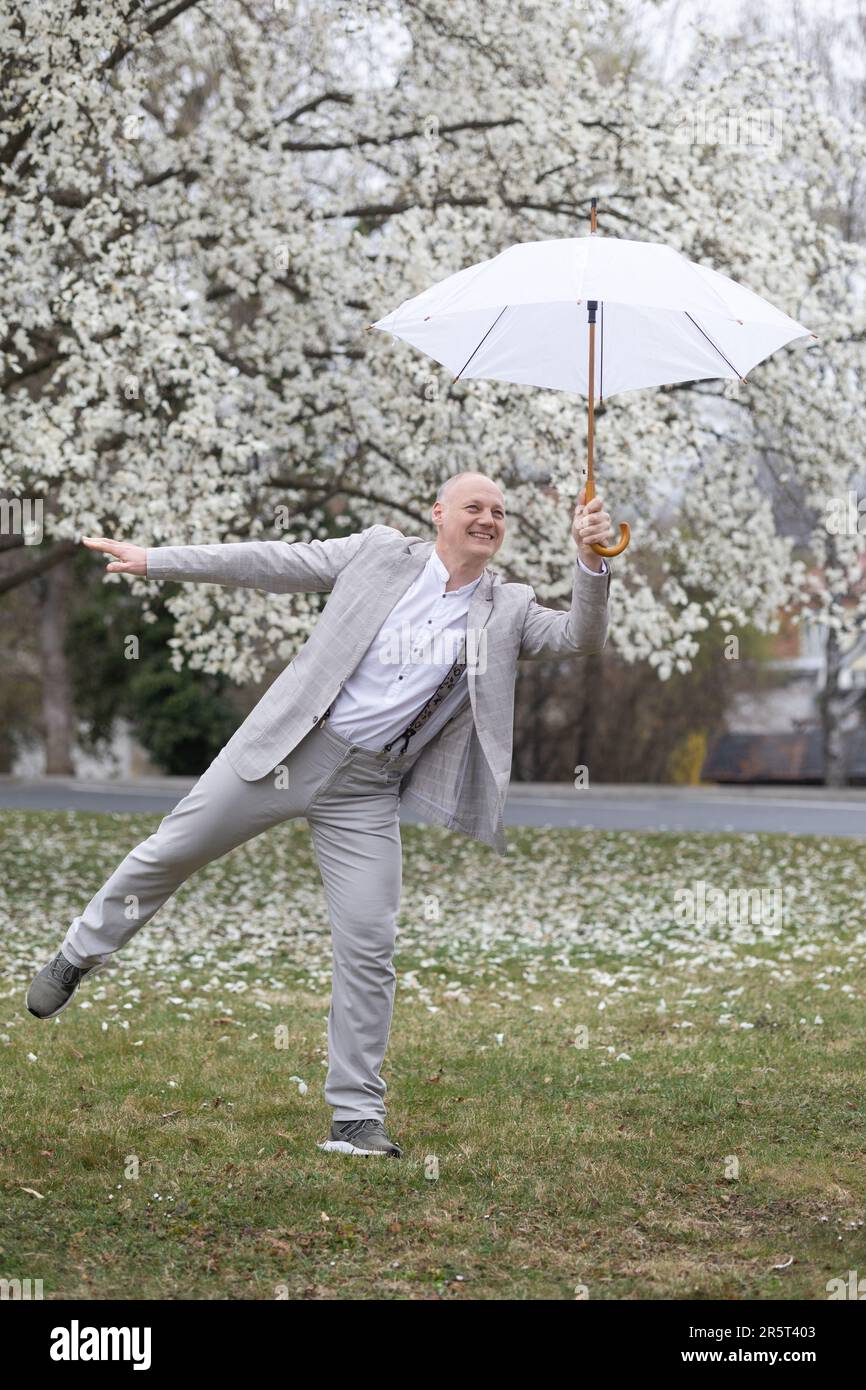 Wunderschöner lächelnder Mann mit Schirm inmitten von weißer blühender Magnolie Stockfoto