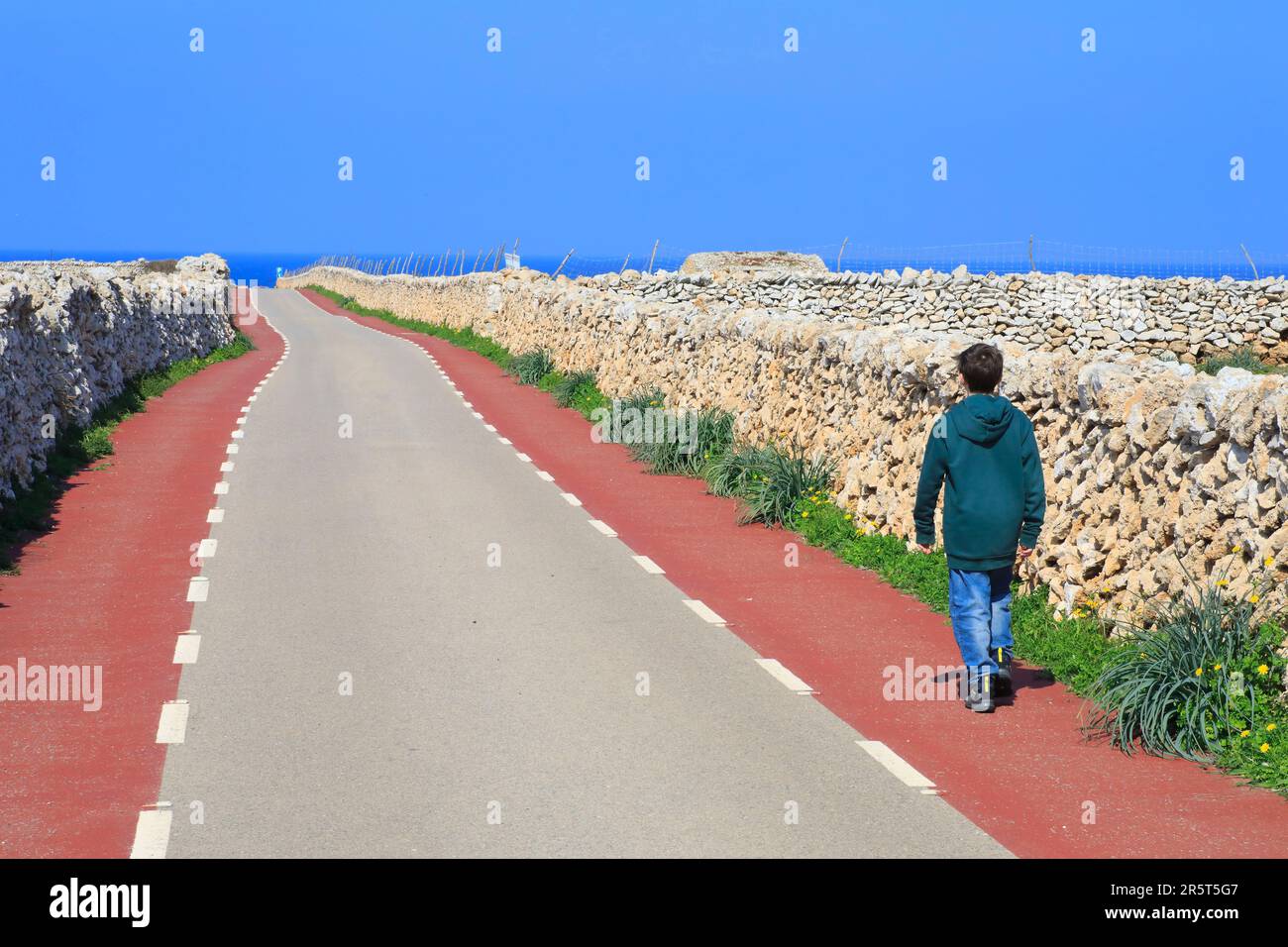 Spanien, Balearen, Menorca, Straße zum Leuchtturm von Punta Nati, trockene Steinmauern mit einem jungen Wanderer Stockfoto