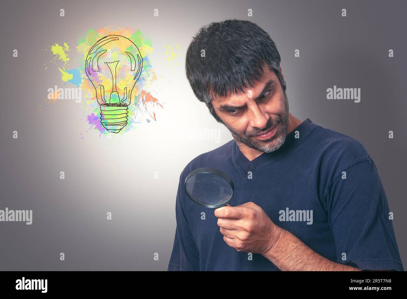 Ein Mann mittleren Alters mit dunklem Haar, der auf der Suche nach Ideen durch eine Lupe blickt, während eine lebendige abstrakte Glühbirne in einer Ecke blinkt, gegen einen Gramm Stockfoto