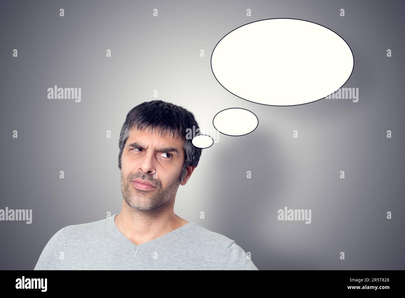 Ein gut aussehender Mann im Vordergrund, mit einem grauen Hintergrund, geschmückt mit weißen Blasen, die Gedanken und Kreativität repräsentieren. Stockfoto