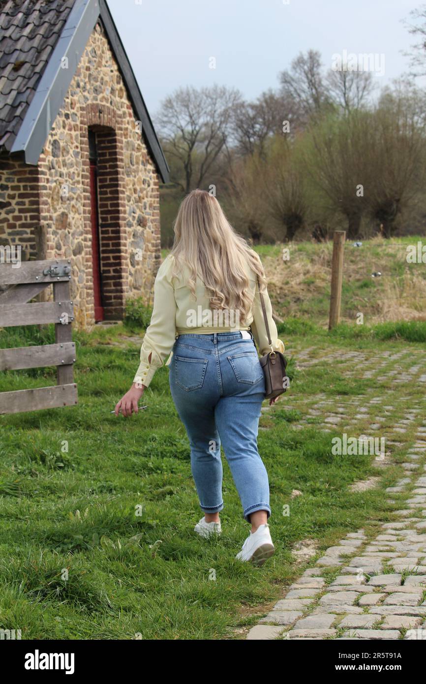 Eine junge Frau, die eine kleine Gasse entlang geht, die von zwei Gebäuden mit üppigem, grünem Gras umgeben ist Stockfoto