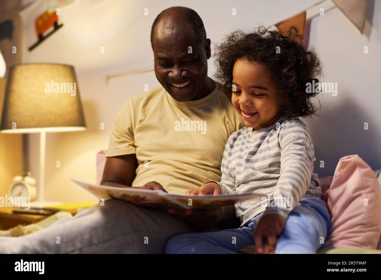 Glücklicher Vater, der seinem kleinen Sohn Bilder im Buch zeigte, während er ihn vor dem Schlafen in der Nacht las Stockfoto