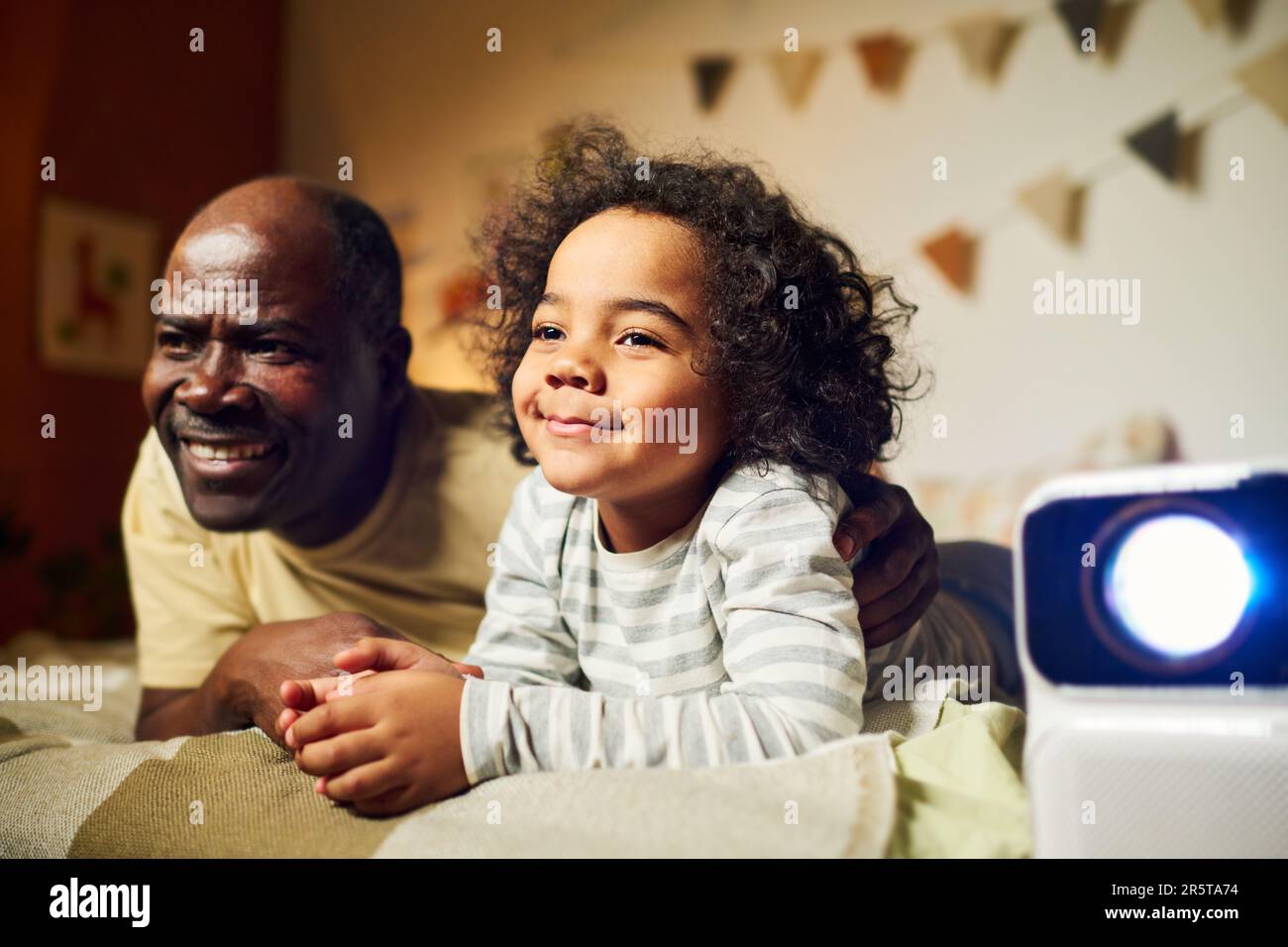 Glücklicher Vater, der zusammen mit seinem kleinen Sohn einen Film auf dem Projektor ansieht, bevor er im Zimmer schläft Stockfoto