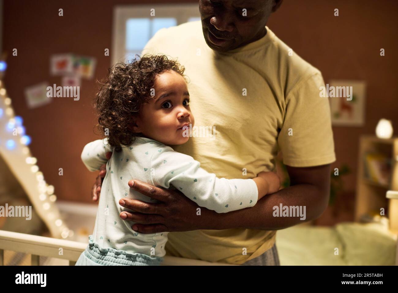 Ein afroamerikanischer Vater, der seinen kleinen Sohn in die Arme nimmt, um ihn einzuschlafen Stockfoto