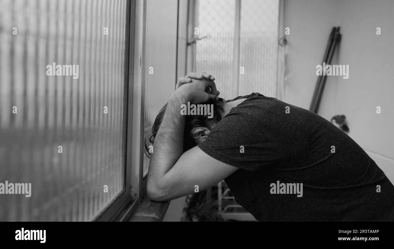 Ein Mann, der zu Hause mit Depressionen kämpft. Dramatische monochromatische schwarz-weiße männliche Person, die an einer psychischen Erkrankung leidet Stockfoto