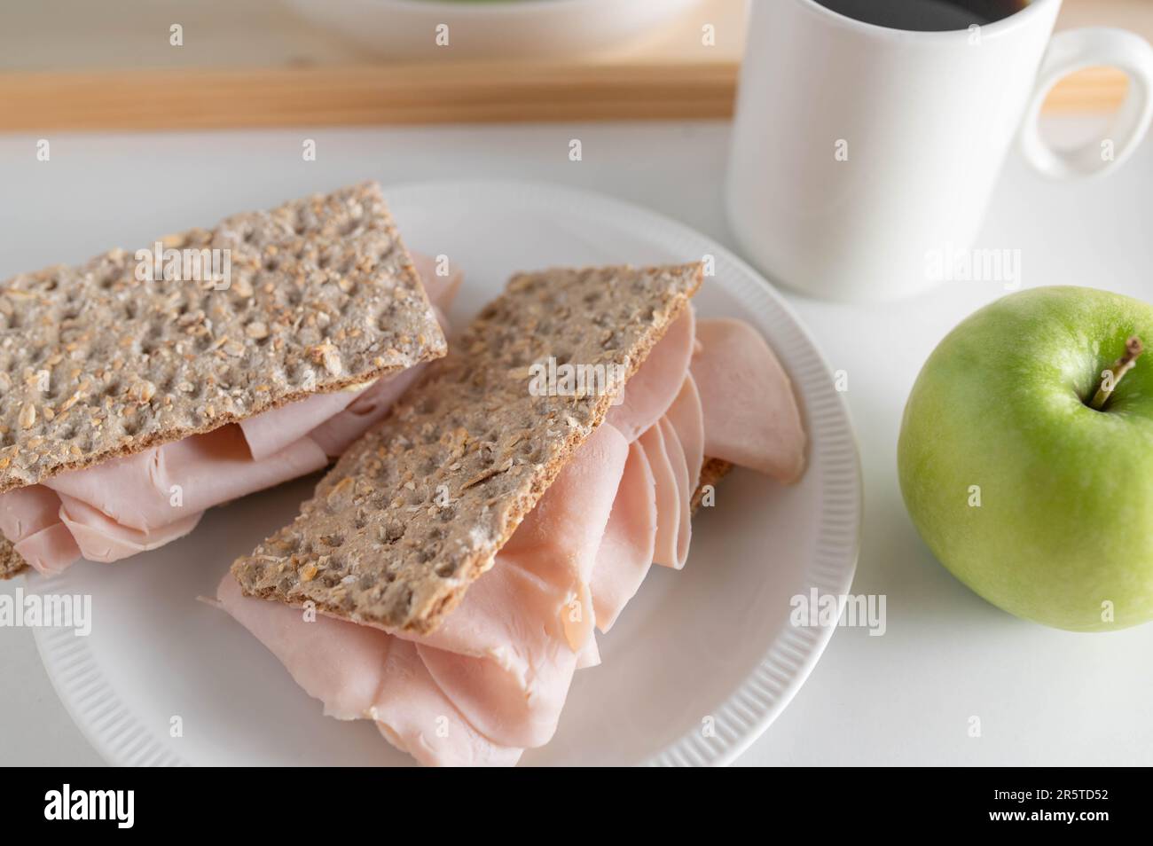 Fettarmes Proteinfrühstück mit Knäckebrot, Hähnchenschinken, grünem Apfel und Kaffee Stockfoto
