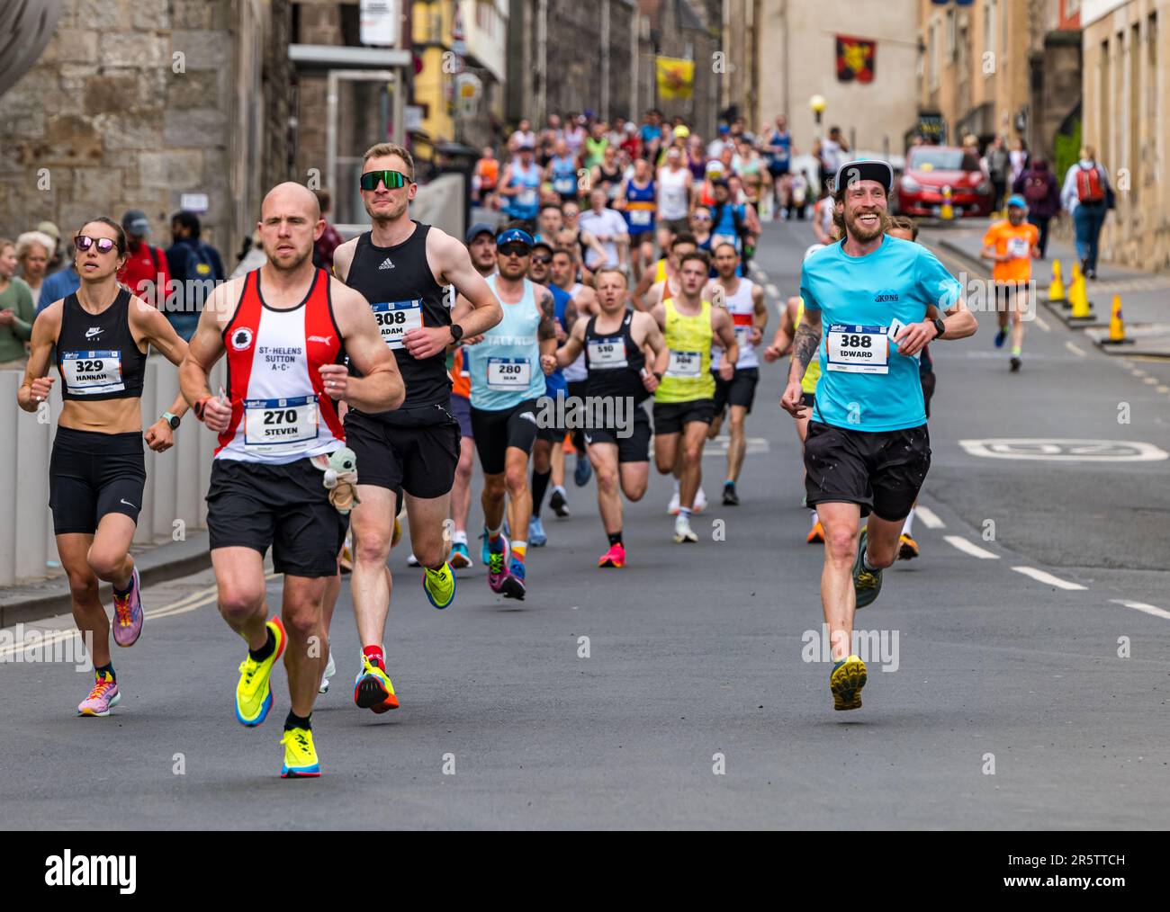 Läufer laufen im Edinburgh Marathon 2023 mit einem lächelnden Teilnehmer, Canongate, Royal Mile, Schottland, Großbritannien Stockfoto