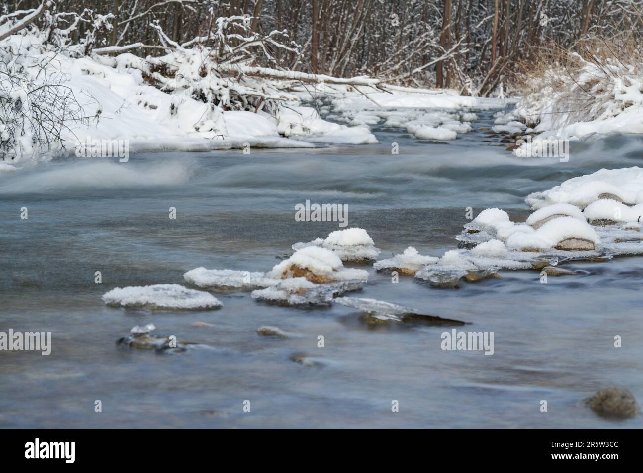 Winterliche Flußoberfläche mit Schneekristallen und Eis, das auf dem Wasser schwimmt - Langzeitfoto, Oberfläche ist seidig glatt Stockfoto