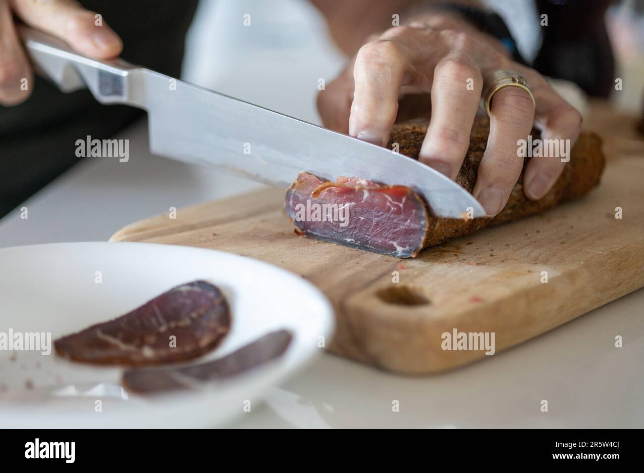 Ein Koch bereitet eine Mahlzeit in einer Küche zu und schneidet Pastirmastücke auf einem Holzbrett Stockfoto