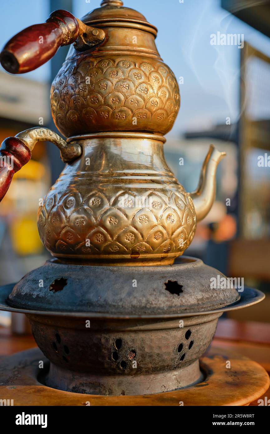 Türkische Teekanne aus graviertem Kupfer, selektiver Fokus. Traditionelle türkische Teekanne mit doppelten Teekannen auf einem Stand mit Kohlen in einem Café, vertikaler Shot, Dampf Stockfoto