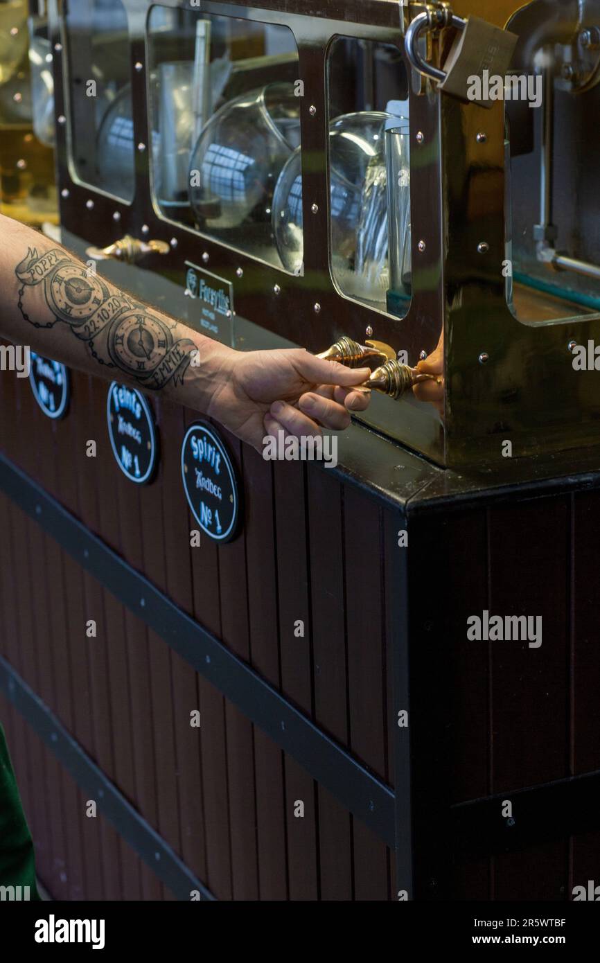 Tätowierter Arm überprüft den Alkoholgehalt im Spirit Safe in der Ardbeg Distillery, Isle of Islay, Inner Hebrides, Schottland, Großbritannien Stockfoto