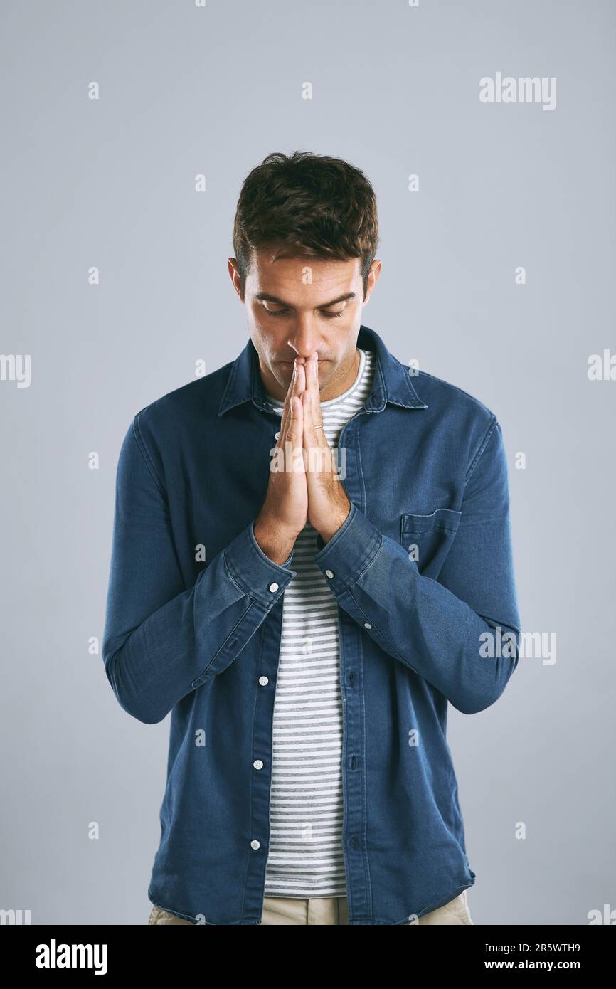 Ich hoffe und bete... ein gutaussehender Mann, der vor einem grauen Hintergrund ängstlich aussieht. Stockfoto