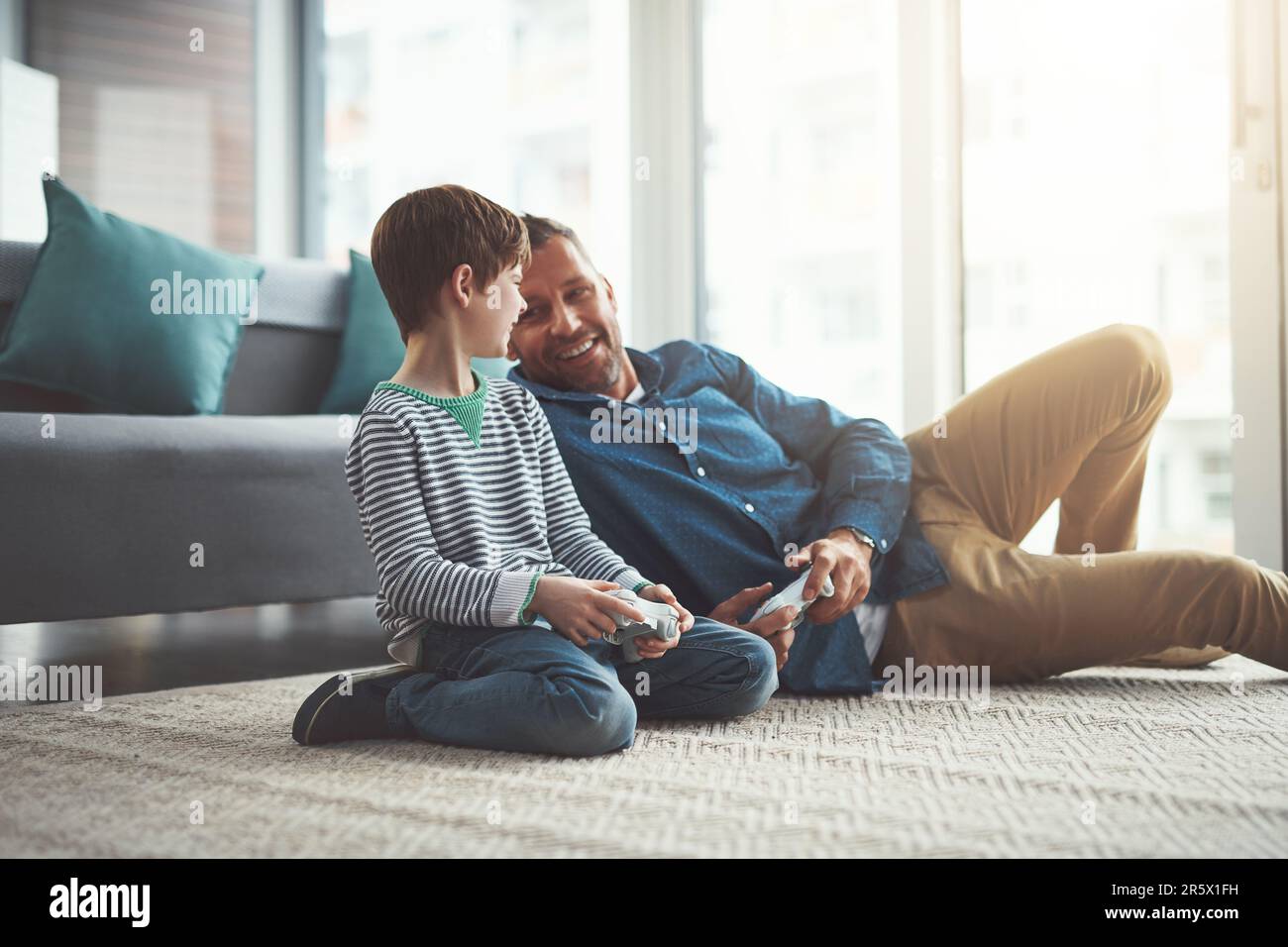 Darf ich das nächste Spiel wählen? Ein fröhlicher kleiner Junge und sein Vater spielen zusammen Videospiele im Fernsehen, während sie auf dem Boden sitzen Stockfoto