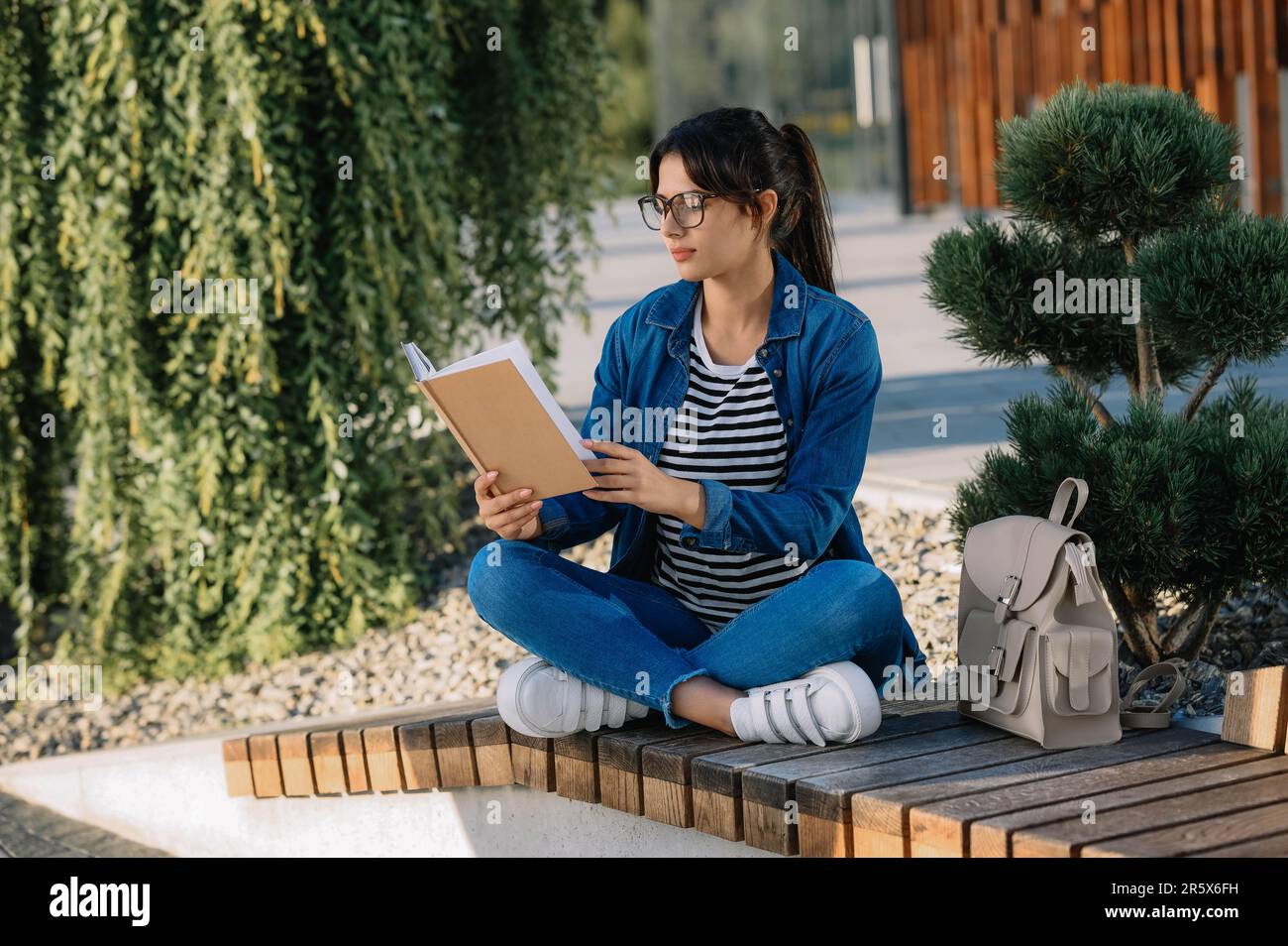 Junge Frau, die draußen auf einer Bank ein Buch liest Stockfoto