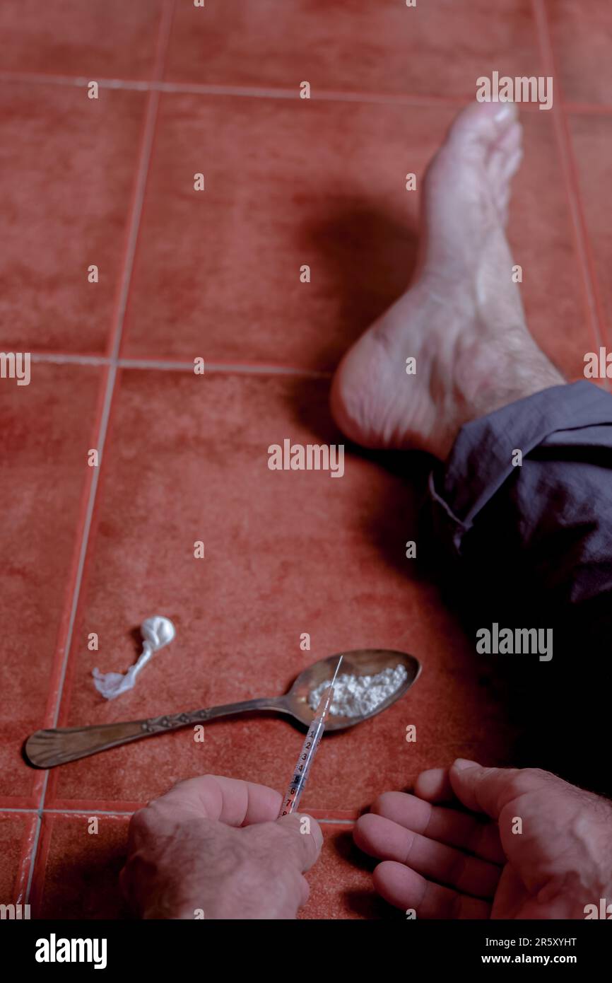 Barfuß sitzender Mann auf dem Boden, der eine Arzneimittelspritze mit einem Löffel heroinhaltig bereitete Stockfoto