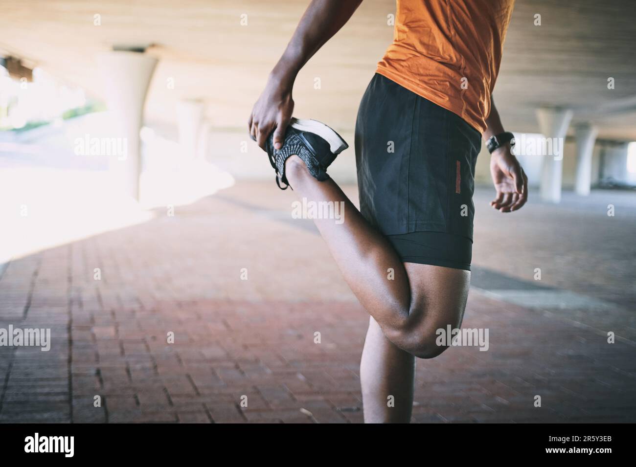 Die Knie der Läufer sind echt, bleib auf der sicheren Seite. Ein Mann, der sich während eines Workouts vor urbanem Hintergrund dehnt. Stockfoto
