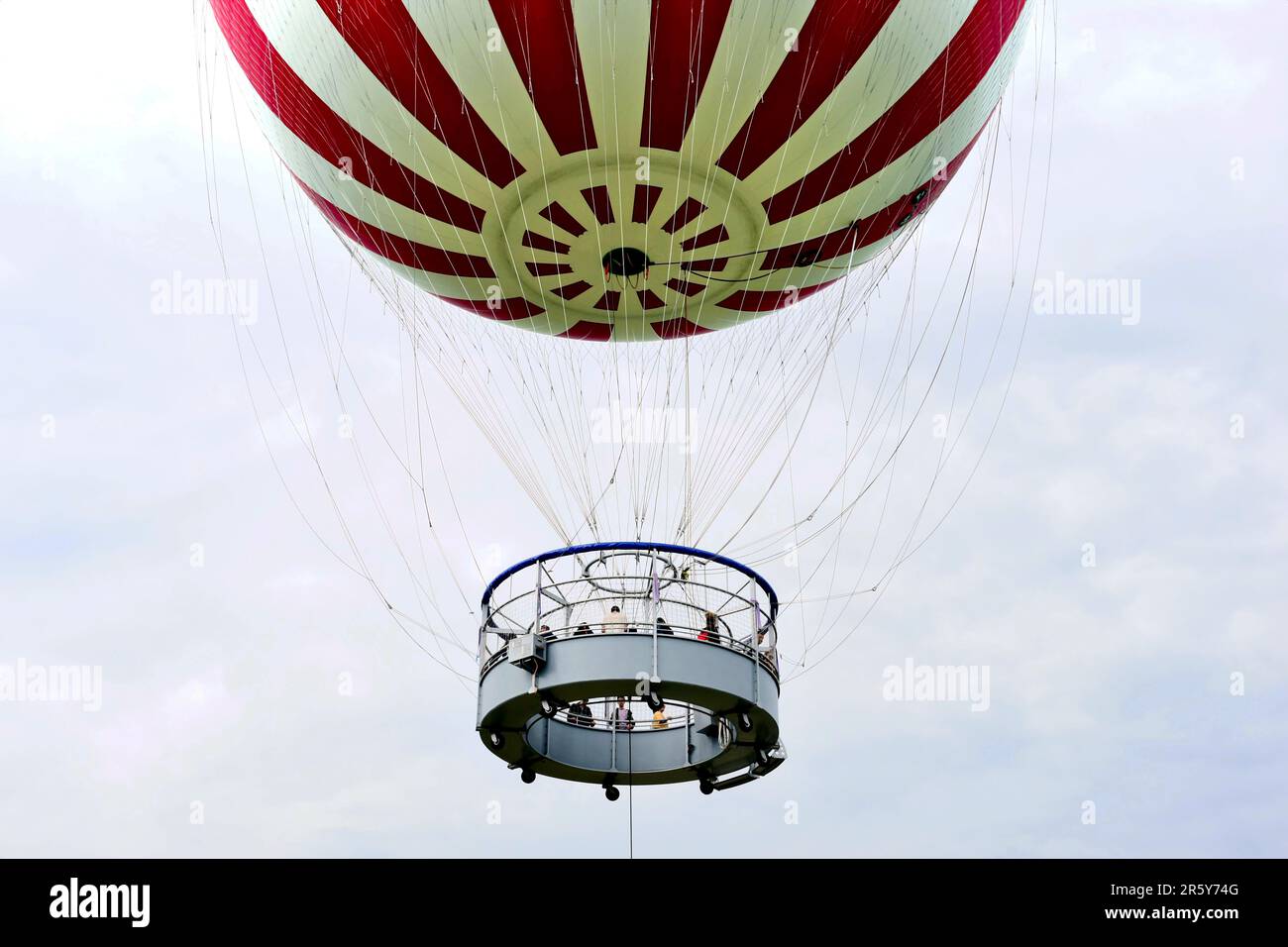 Schwebende rot-weiße Ballon-Nahaufnahme. Hängekorb und Aussichtsplattform mit Menschen. Aufhängungsseile. Besichtigungstour in Budapest Stockfoto