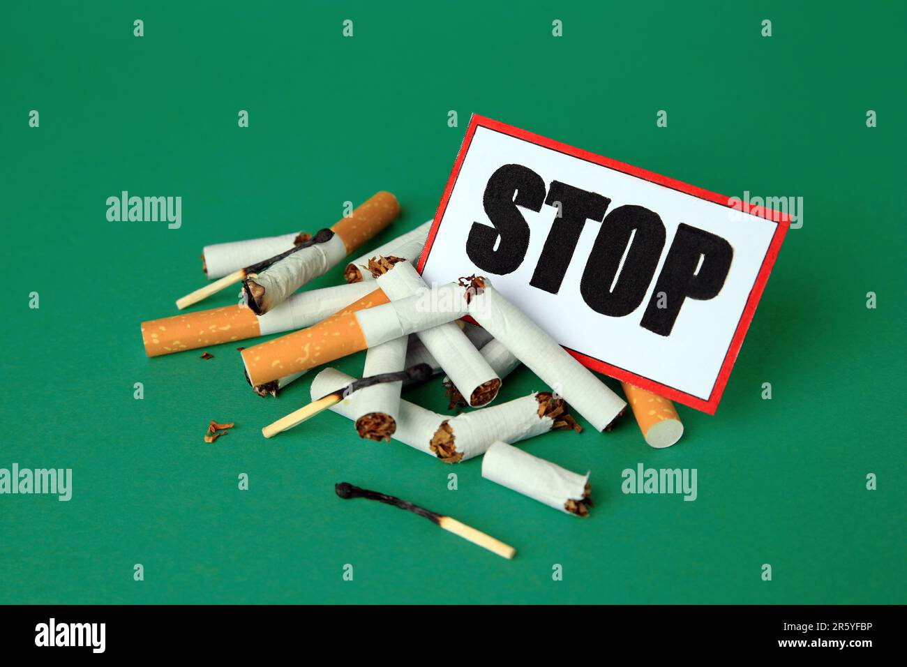 Karte mit Wort Stop, Zigarettenstummeln und verbrannten Streichhölzern auf grünem Hintergrund. Rauchverbot-Konzept Stockfoto